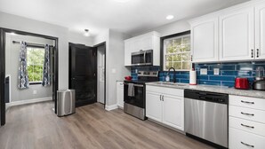 A modern kitchen with white cabinets, stainless steel appliances, and a blue tiled backsplash.