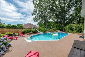 Ein Garten mit Schwimmbad, roten Liegestühlen, einer Rutsche und einem Baum.