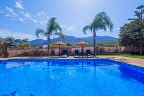 A swimming pool with lounge chairs and palm trees, surrounded by a landscaped area with mountains in the background.