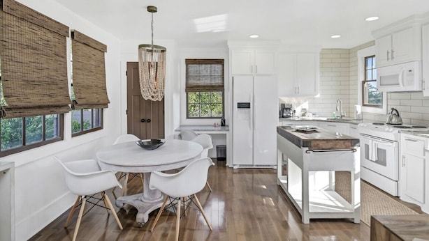 Una cocina moderna con armarios blancos, una isla central y un comedor con sillas blancas.