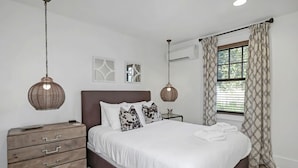 Un dormitorio con una cama grande, mesitas de noche, un aparador y una ventana con cortinas estampadas.