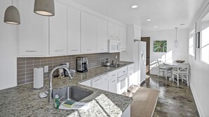 A modern kitchen with white cabinets, granite countertops, and pendant lighting.