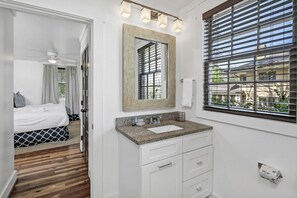 Un baño moderno con encimera de granito, un espejo grande y una ventana con persianas.