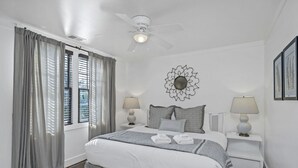 A bedroom with a bed, two bedside tables, a ceiling fan, a wall decoration, and a window with curtains.