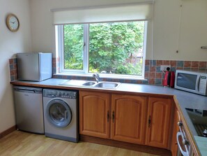 A compact kitchen with a washing machine, a microwave, and a sink under a window. - Bo Nan Taigh Cottage (Aberfoyle)
