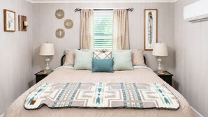 Un dormitorio con cama, dos mesitas de noche, ventana con cortinas, espejos en la pared y un equipo de aire acondicionado.
