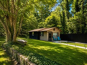 A small, single-story house with a sloped roof, a front porch with two chairs, and a fenced backyard. - Escape to the Smokies! Tiny House Cabin-Special - 4 Night Min w/free cleaning! (Gatlinburg)