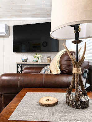 Un salon avec un canapé en cuir marron, une table basse en bois, une lampe décorée de motifs de bois de cerf et un téléviseur fixé au mur.