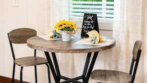 Una mesa redonda de madera con dos sillas, un cubo de girasoles y un cartel de bienvenida.