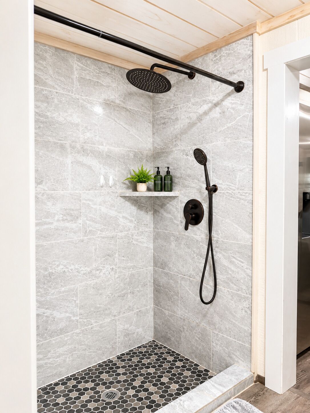A shower area with a rain showerhead, handheld showerhead, and a small shelf with toiletries.