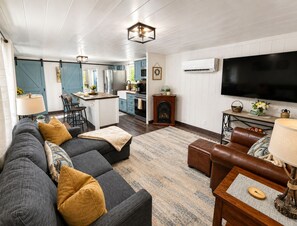 A modern living room with a sectional sofa, a leather armchair, and a television. - Escape to the Smokies! Tiny House Cabin-Special - 4 Night Min w/free cleaning! (Gatlinburg)