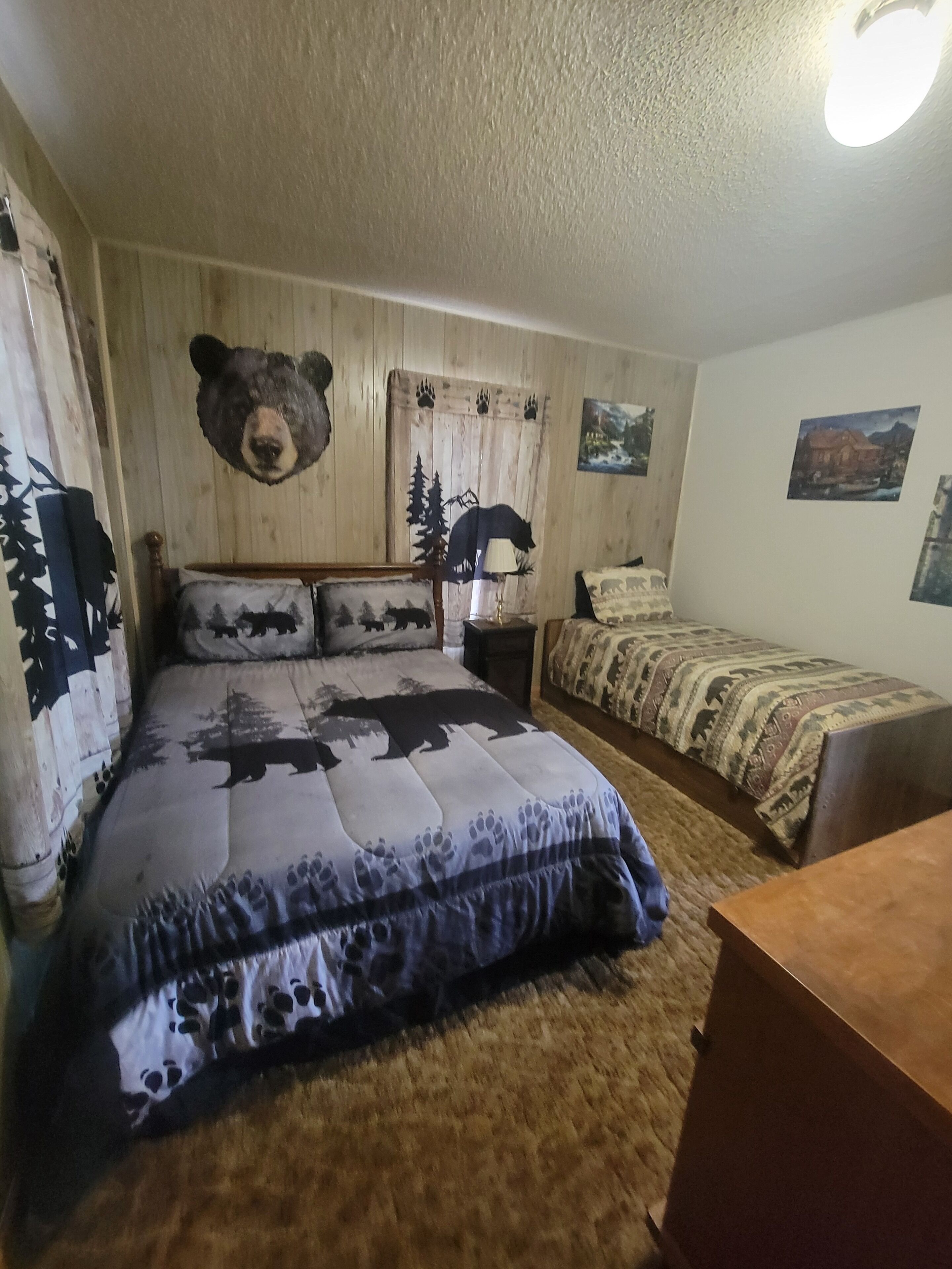 Um quarto com cama, mesa de cabeceira, luminária, cômoda e parede decorada com cabeça de urso.