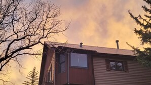 A two-story house with a wooden exterior and a metal roof. There are two windows on the ground floor and a door. - Hot tub fun,  warm up by the fire pit, after a long day of all day play!  (Collbran)