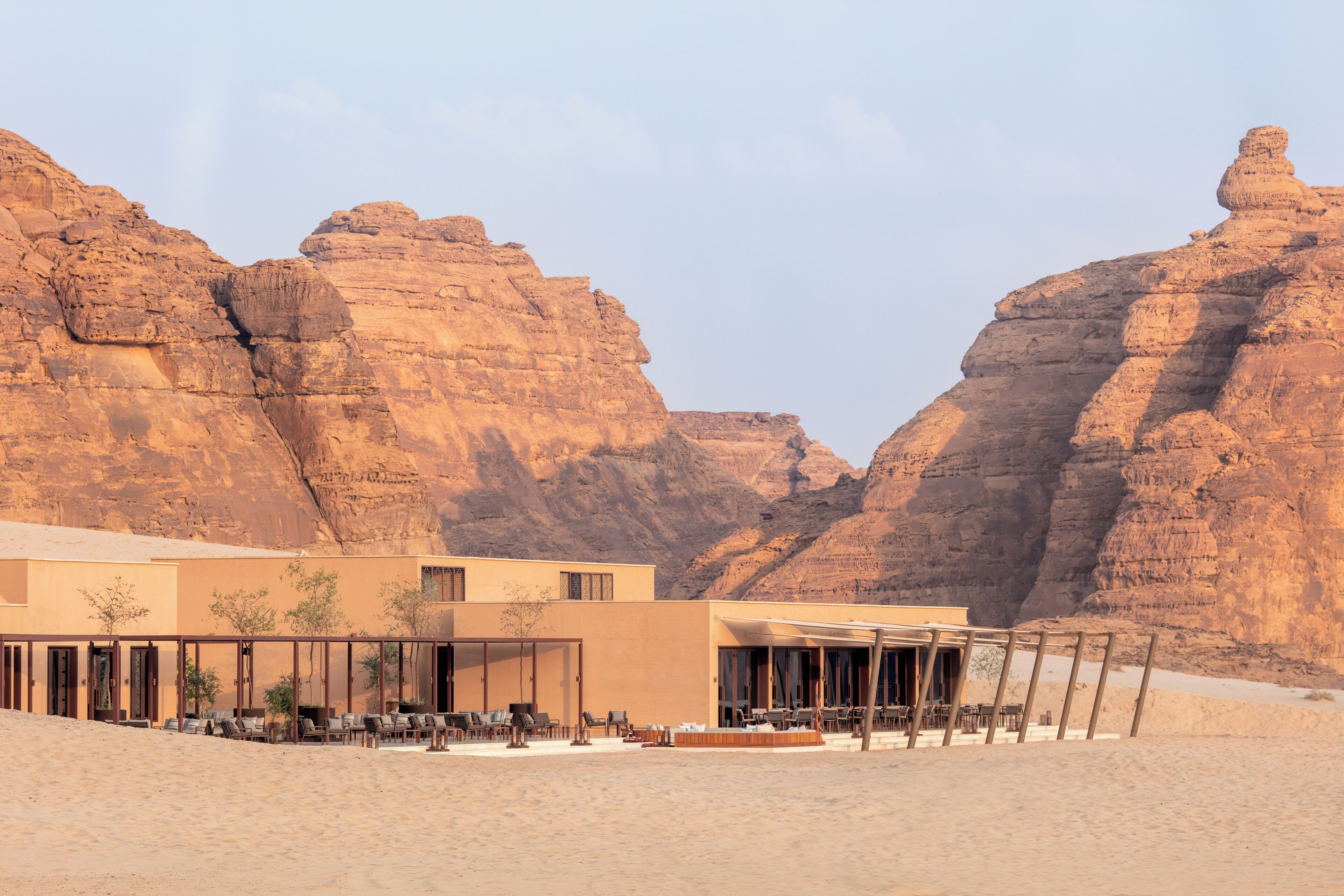Un resort en el desierto con un edificio moderno, mesas al aire libre y vistas a acantilados rocosos.