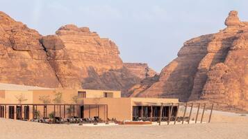 Un resort en el desierto con un edificio moderno, mesas al aire libre y vistas a acantilados rocosos.