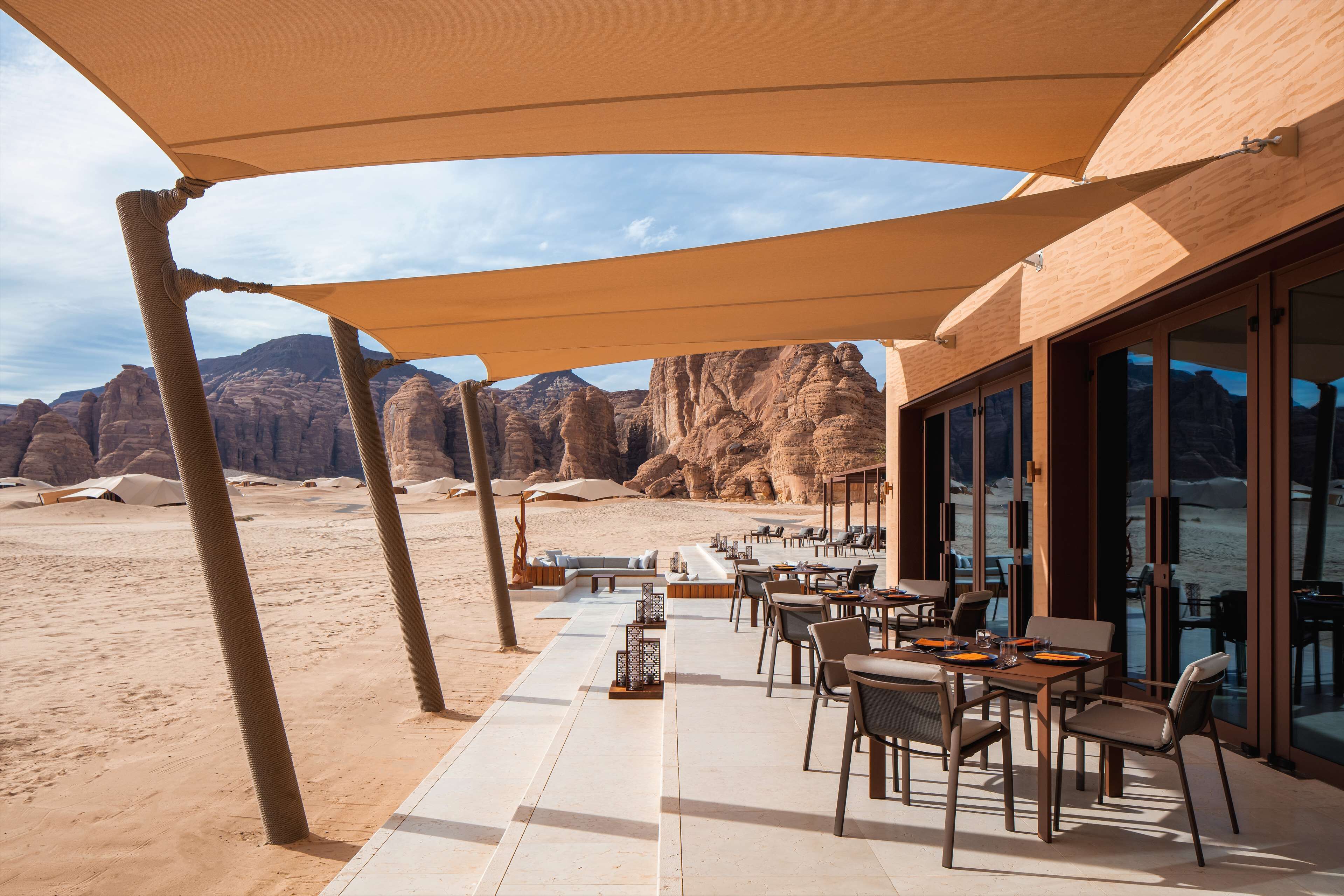 An outdoor dining area with tables and chairs, overlooking a desert landscape with rock formations.