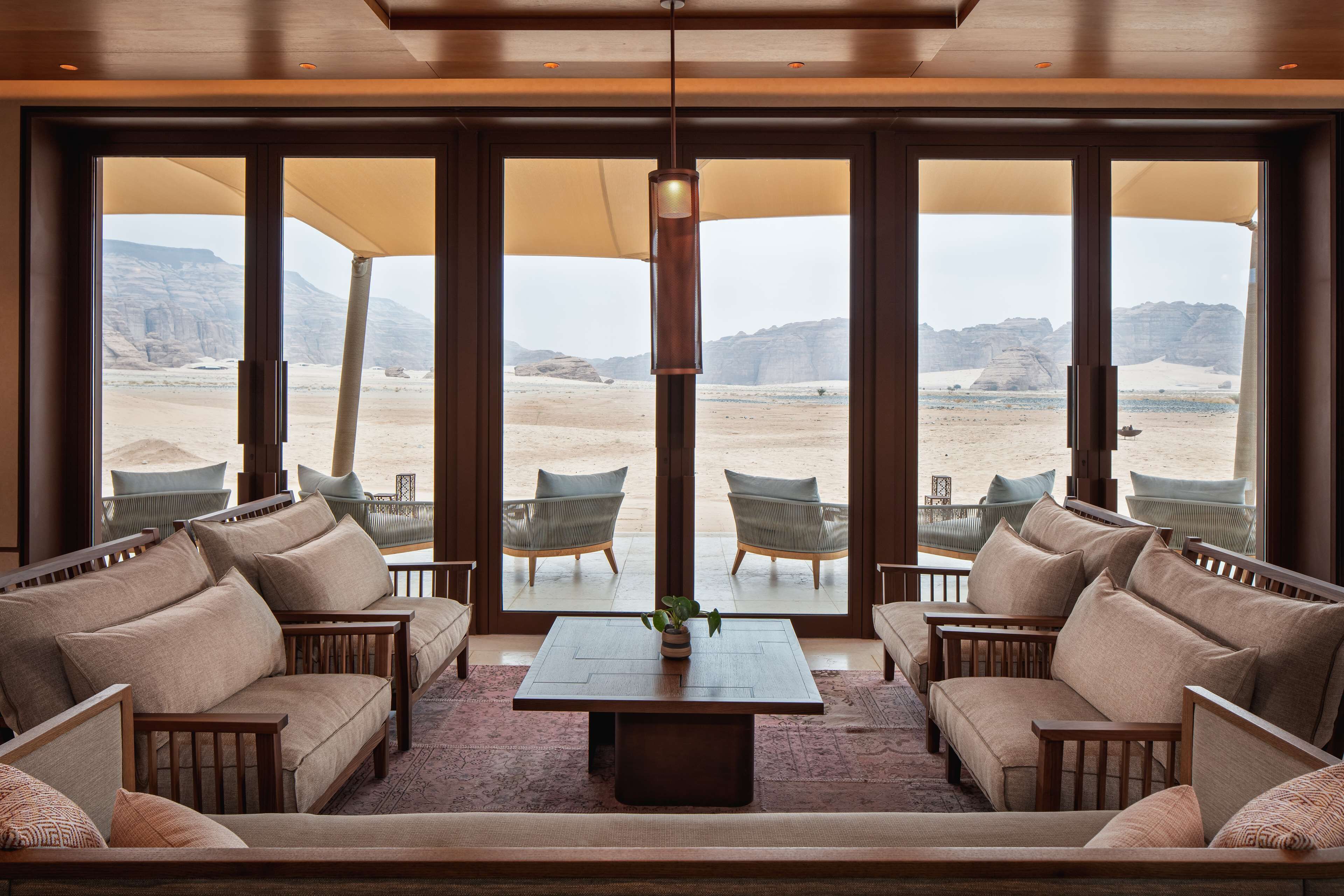 Amplia habitación con un gran ventanal con vistas a un paisaje desértico. Hay varias zonas de estar con sofás y sillones.