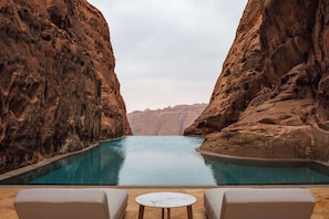 A pool with a view of rocky cliffs. There are two lounge chairs and a small table. - Banyan Tree AlUla (Al-'Ula)