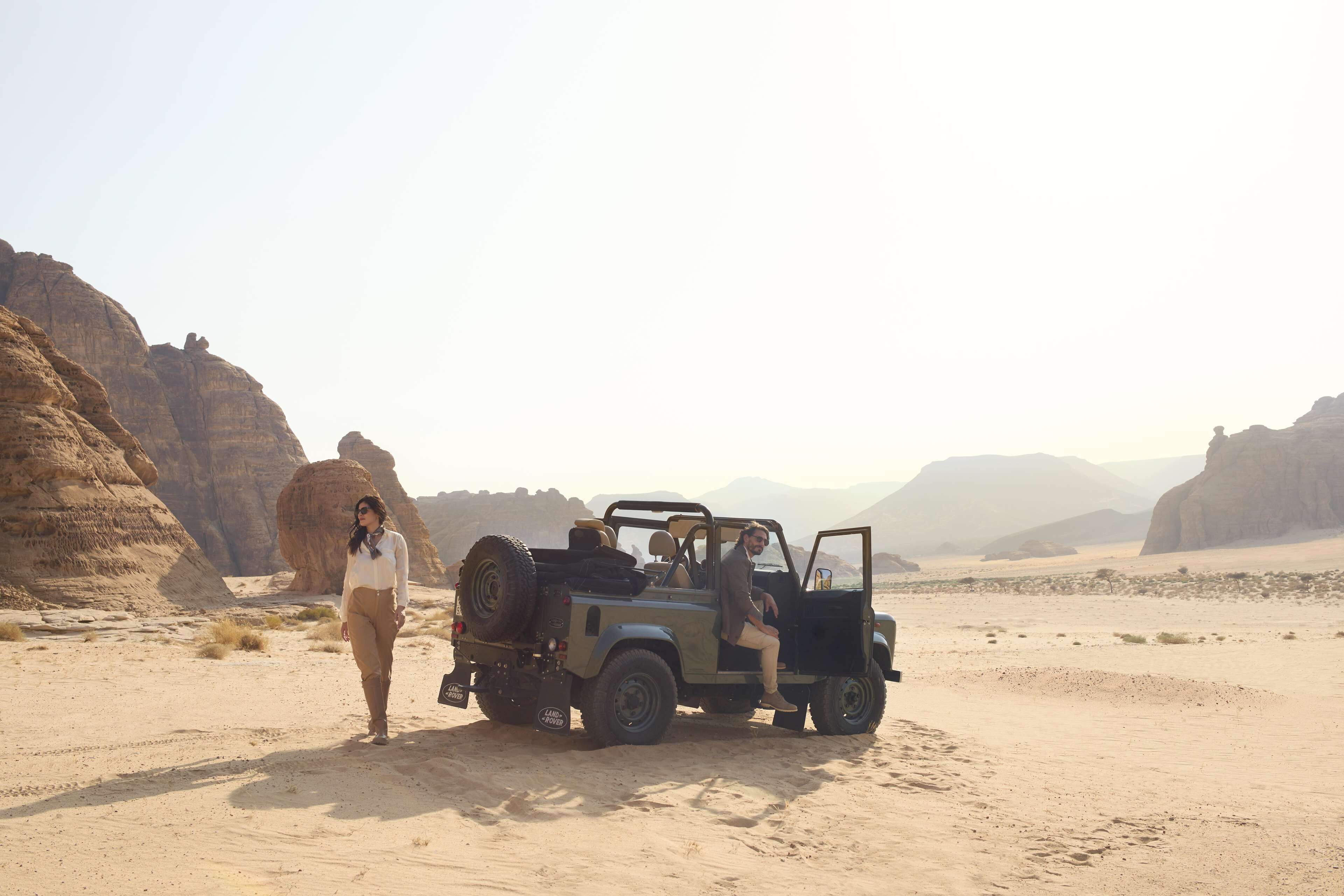 A desert landscape with a vehicle and a person standing beside it.