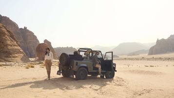 A desert landscape with a vehicle and a person standing beside it.
