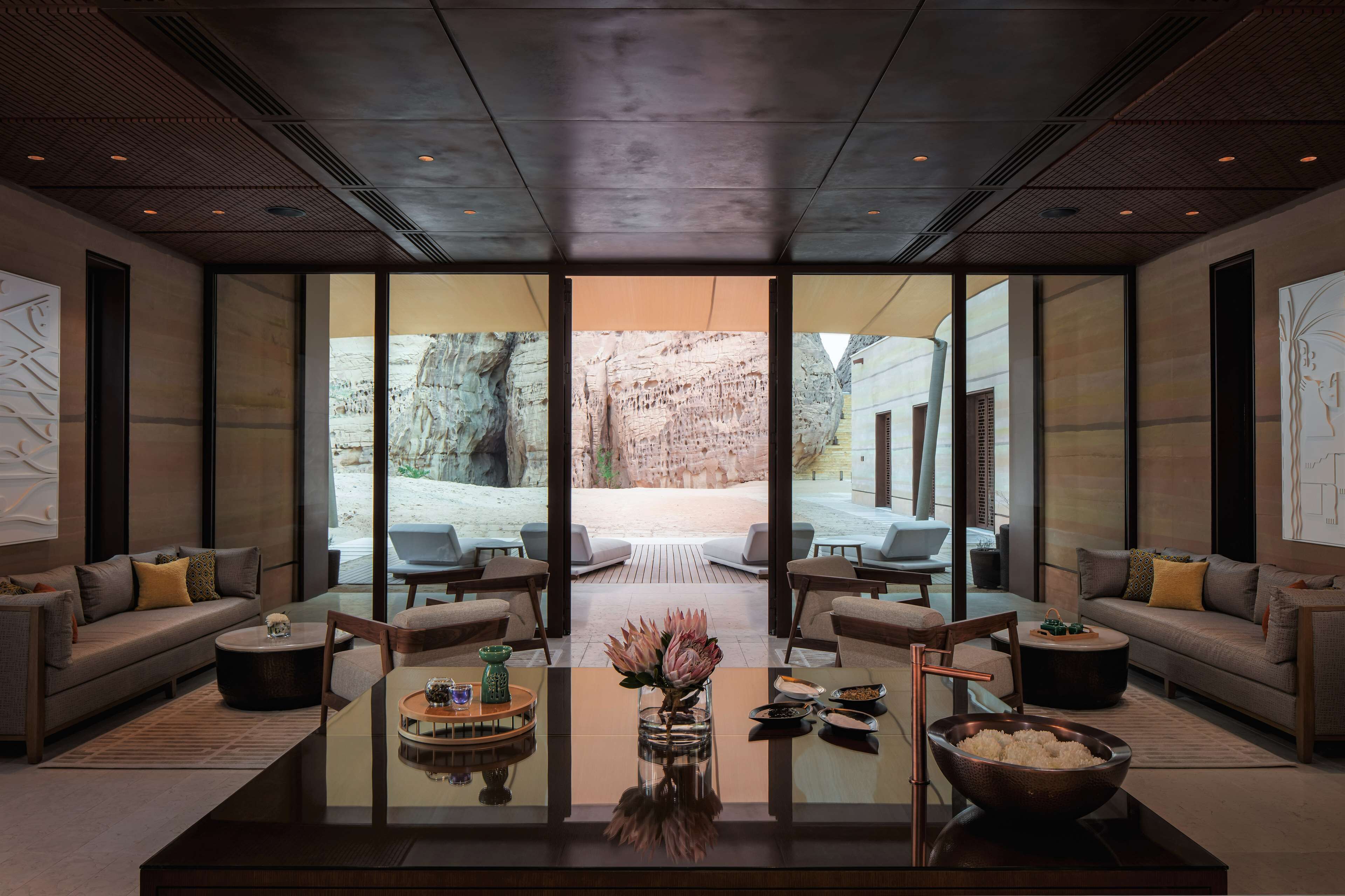 A modern interior with a glass wall leading to an outdoor patio, furnished with sofas and a coffee table.