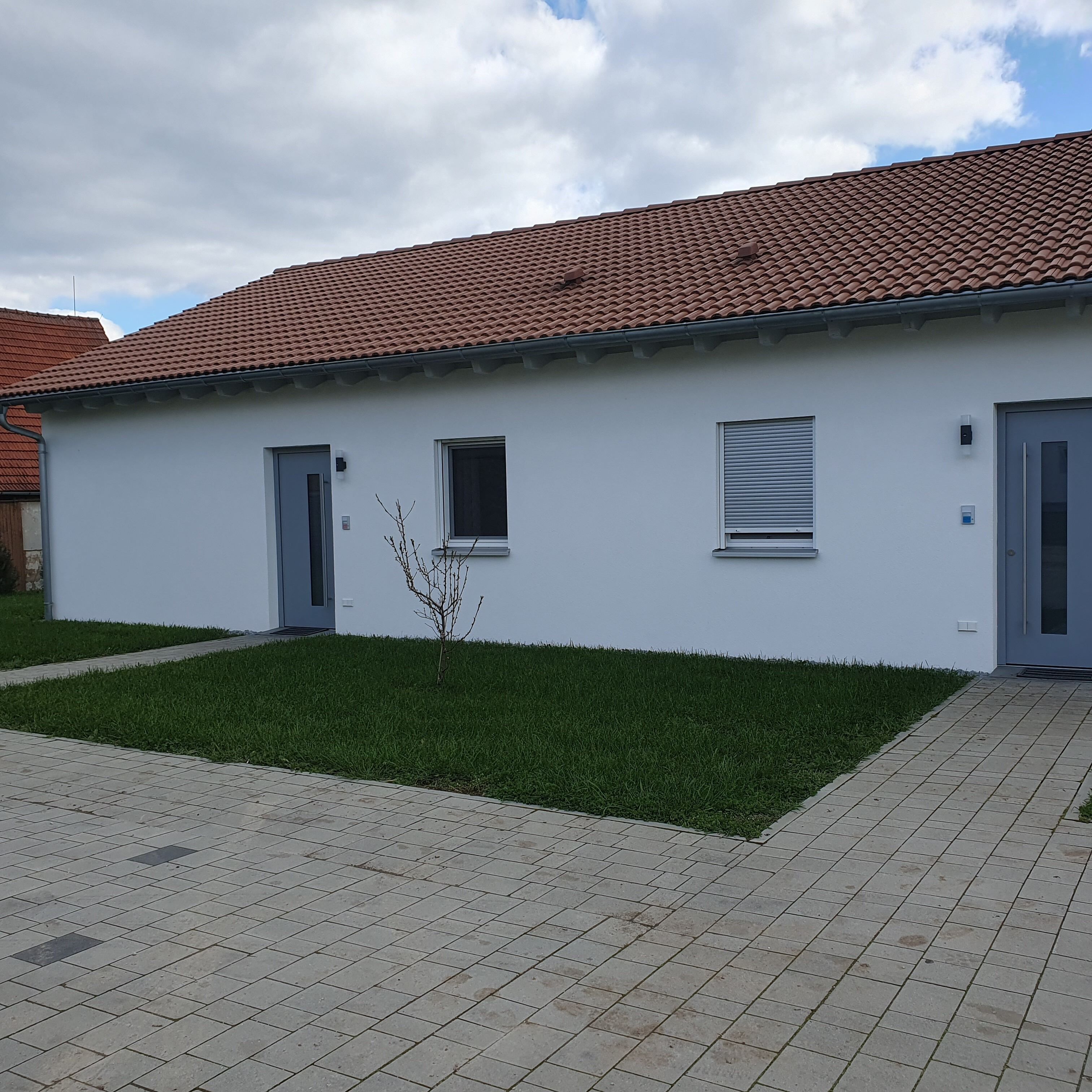 A modern two-story building with a tiled roof, a small front yard with grass, and a paved entrance area.
