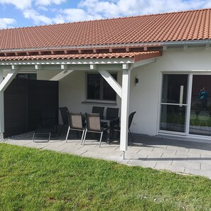 Un patio cubierto con techo de baldosas, una mesa con sillas y una puerta corrediza de cristal.