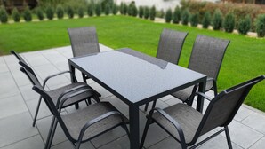 Een rechthoekige tuintafel met vier stoelen, elk met een net rugleuning, op een betegeld terras.
