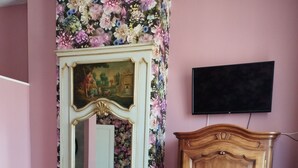 Et værelse med blomstret tapet, et træskab, en blå polstret stol og en pejs med et spejl over.