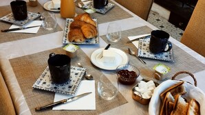 En morgenmadsopsætning med et bord dækket til to personer, med croissanter, smør, marmelade og ristet brød.