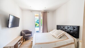Quarto com cama, televisão na parede, uma cadeira e um banco de madeira.