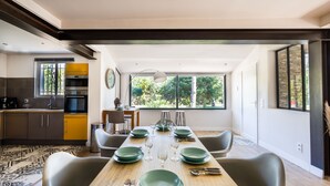 Uma sala de jantar moderna com uma mesa de madeira posta para seis pessoas, rodeada por cadeiras cinzentas.