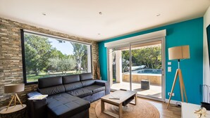 Uma sala de estar moderna com um sofá seccional, uma mesa de centro e vista para uma piscina através de grandes portas de vidro.