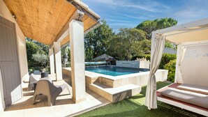 Uma área de piscina com pergolado de madeira, mobiliário de exterior e um espaço de descanso coberto.