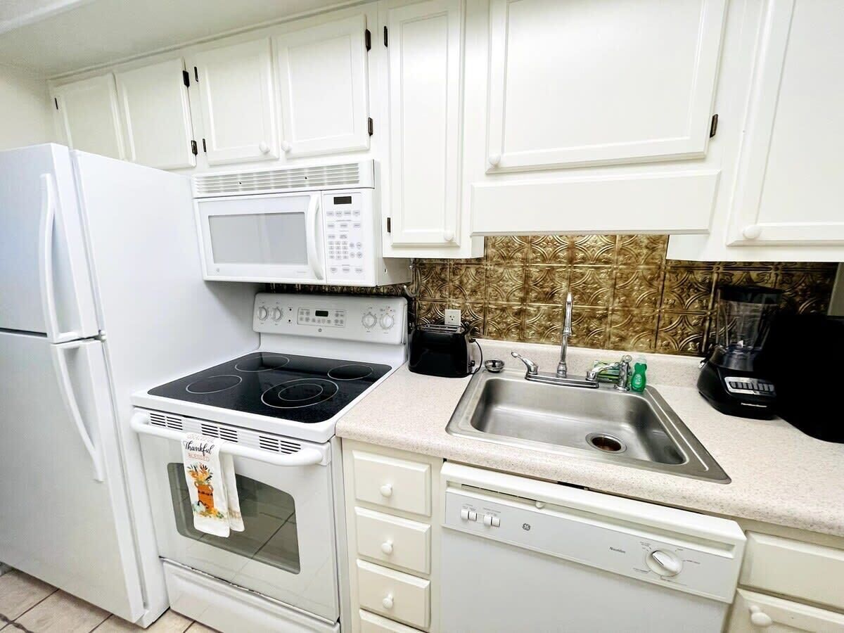 A kitchen with white cabinets, a microwave, stove, dishwasher, and a sink.