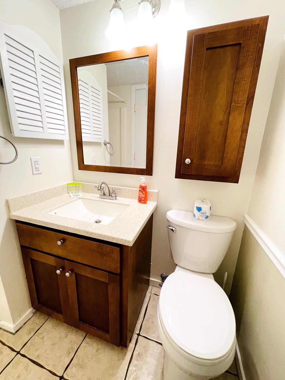 A bathroom with a sink, mirror, toilet, and wooden cabinet.