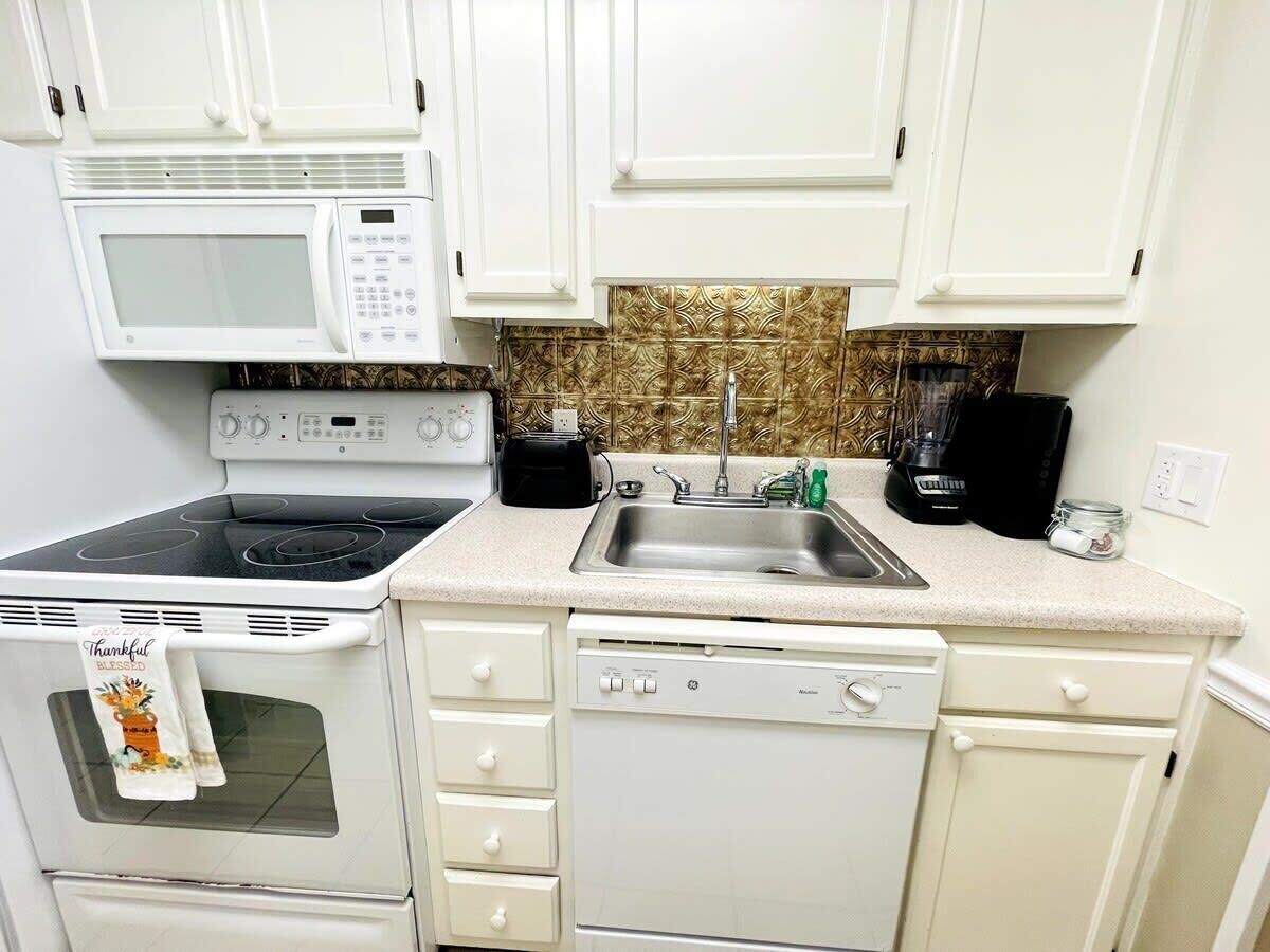 A compact kitchen with white cabinets, a microwave, stove, sink, and dishwasher.