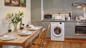 A kitchen with a wooden table set for dining, a washing machine, and modern appliances. - The Old Butcher's Shop (Wereham, near King&rsquo;s Lynn)