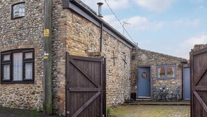 A stone building with a wooden gate, a small door, and a window with curtains. - The Old Butcher's Shop (Wereham, near King&rsquo;s Lynn)