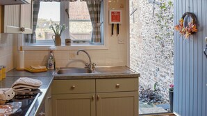 A kitchen with a sink, a window with curtains, a fire blanket sign, and a decorative wreath. - The Old Butcher's Shop (Wereham, near King&rsquo;s Lynn)
