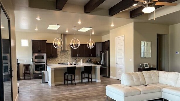 A spacious living room with a large white sectional sofa, a kitchen with dark wood cabinets and stainless steel appliances, and a ceiling fan. - Purple Sage Garden Retreat (Las Cruces)