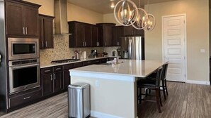 A modern kitchen with dark wood cabinets, stainless steel appliances, a central island with seating, and pendant lighting. - Purple Sage Garden Retreat (Las Cruces)