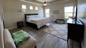 A bedroom with a bed, a desk, a chair, a bench, a standing fan, and a window. - Purple Sage Garden Retreat (Las Cruces)