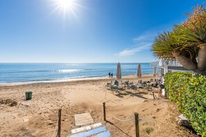 A beach with a seating area, umbrellas, and a palm tree. - Alvarito Playa | Beach Apartment in Marbella (Marbella)