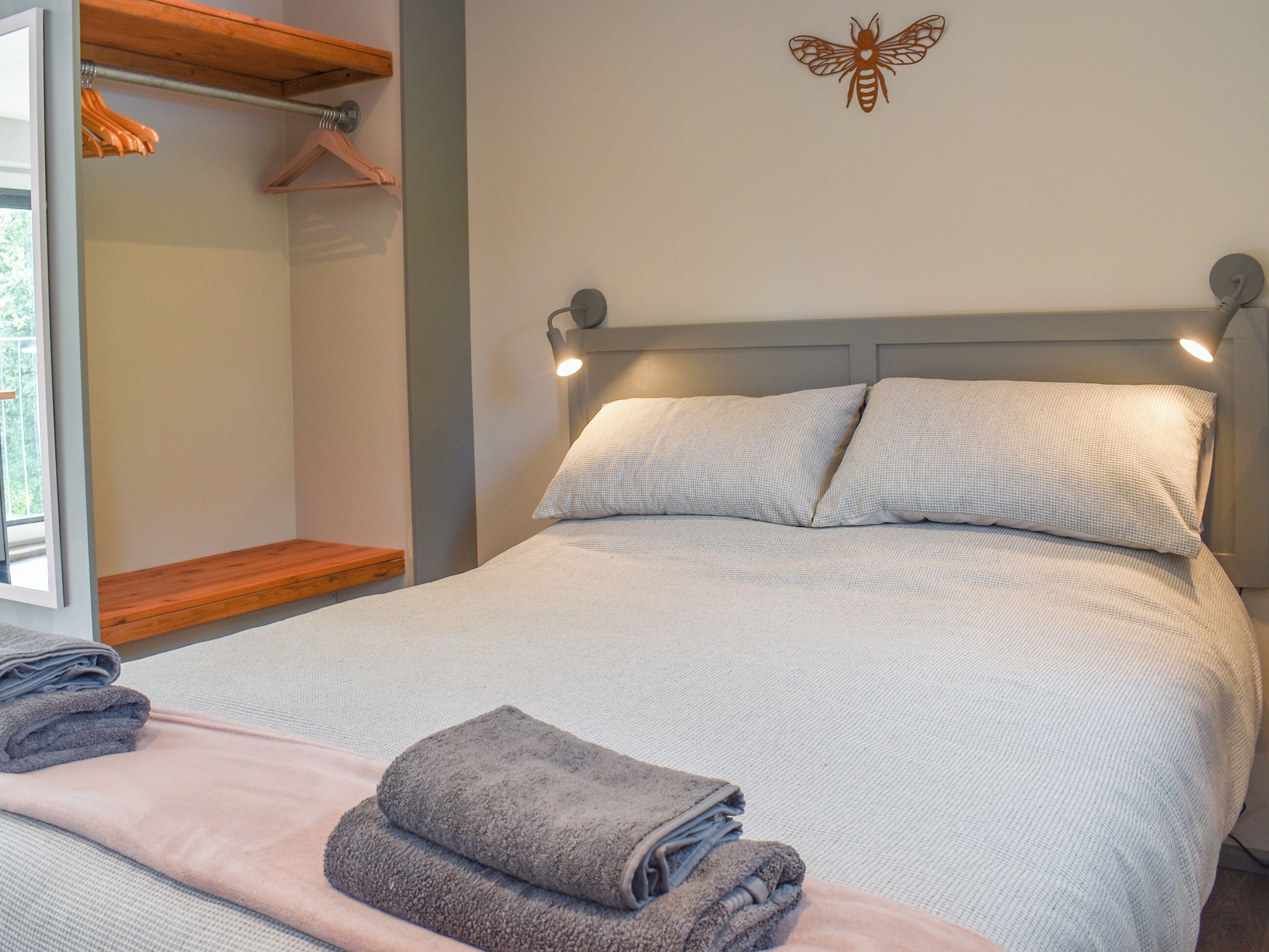 A neatly made bed with pillows, a bedside table, a wall-mounted light, and a butterfly decoration.