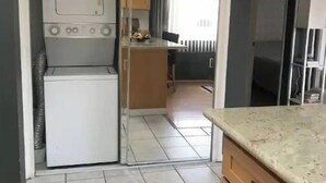 A compact kitchen with a built-in washer and dryer, wooden cabinets, and a tiled floor. - Aloha Waikiki! (Honolulu)