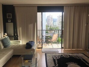 Un salon moderne avec un canapé, une table basse en verre et une vue sur un balcon aménagé avec du mobilier d’extérieur.