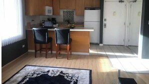 A compact kitchen with wooden cabinets, a white refrigerator, and a small island with two chairs. - Aloha Waikiki! (Honolulu)