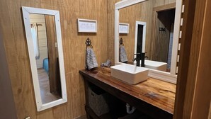 Een houten badkamer met een witte wasbak, een grote spiegel en een handdoekhouder.