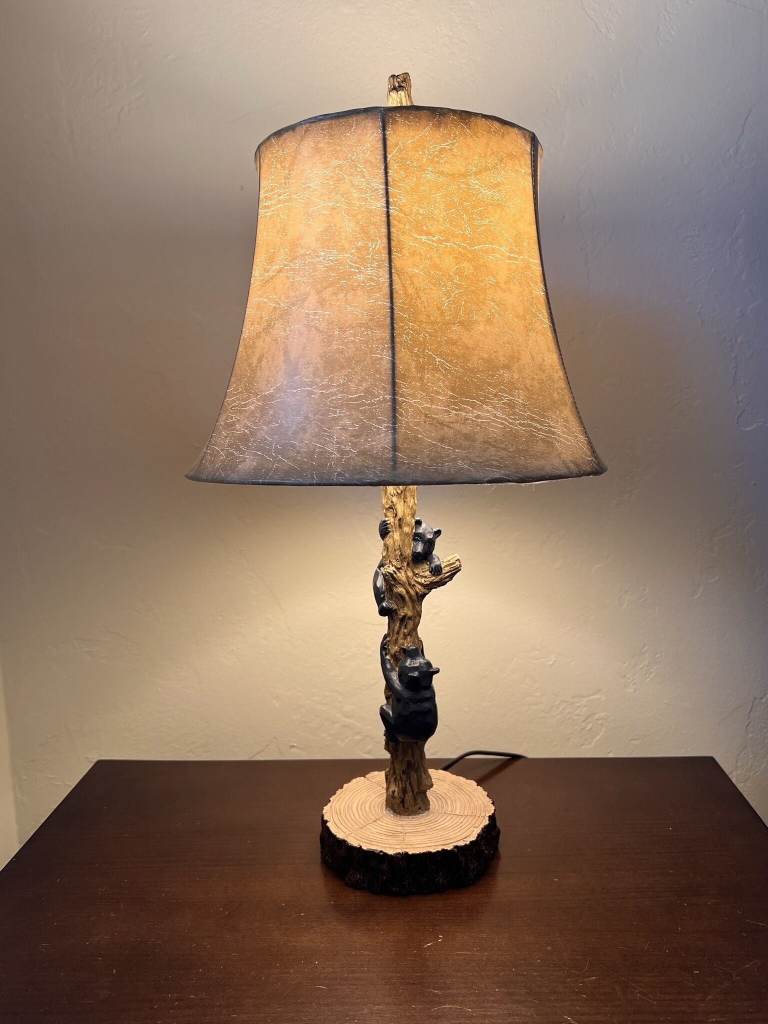 Een lamp met een gestructureerde lampenkap en een houten voetstuk waarop een beerfiguur staat.